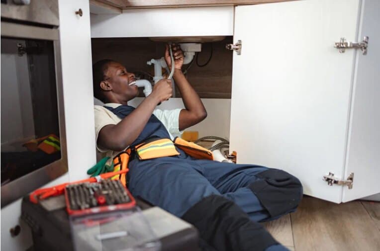Plumber repairing pipes under a kitchen sink